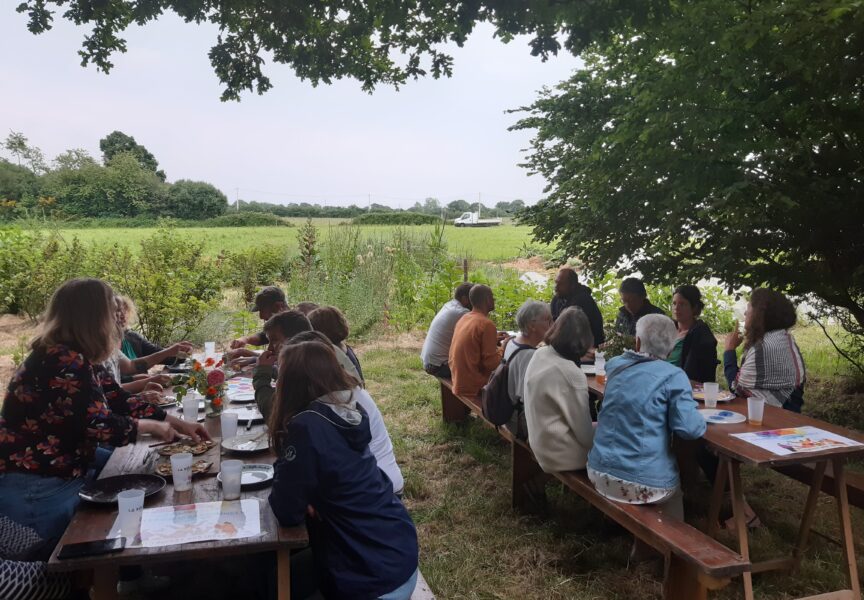 Deux groupes de personnes partagent un moment convivial dehors autour de grandes tables. Ils discutent et partagent un repas.
